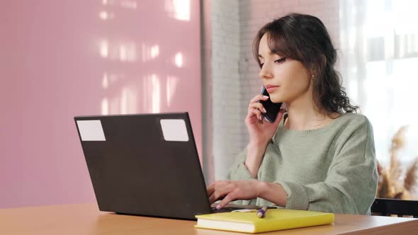 Girl Sitting at Laptop in Her Living Room Talking on Phone and Writing Notes