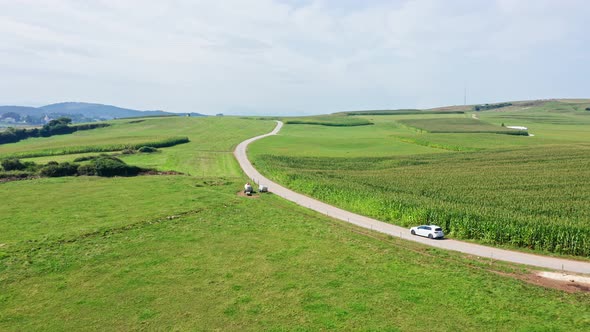 Aerial Top Notch Drone flies above Alfoz de Lloredo fields, Cantabria, North of Spain, while a car t