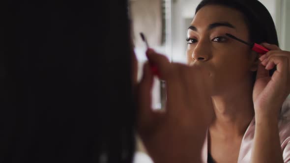 Mixed race gender fluid person standing in bathroom and using mascara