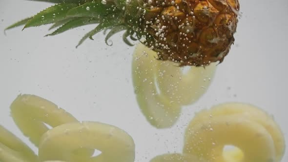 Tropical Fruit Pineapple and Slices Falling Into Water with Splash Air Bubbles on White Background