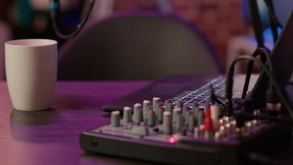 Selective Focus on Laptop Keyboard and Knobs of Audio Mixer on Podcasting Desk