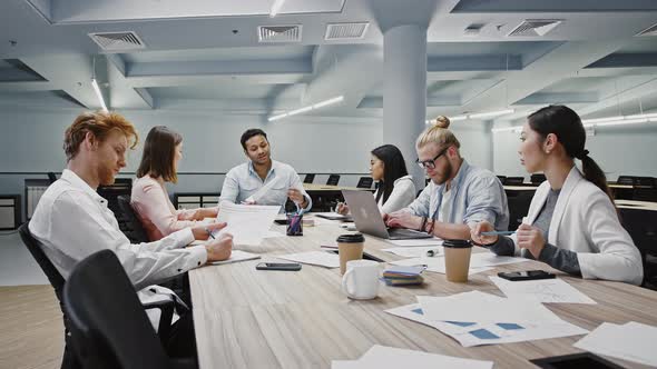 Manager Discussing Details of New Startup with Diverse Colleagues Sitting at Table in Modern Office