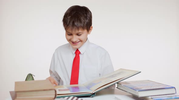 Smiling Caucasian School Kid Folding Pages of Big Atlas Sitting at Table on White Background