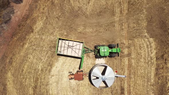Tractor pulls up to a grain silo to unload its cargo of harvested corn - aerial straight down view