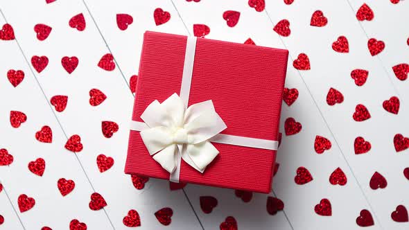 Boxed Gift Placed on Heart Shaped Red Sequins on White Wooden Table