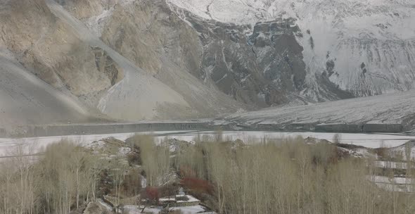 Aerial Over Winter Trees To Reveal Frozen Lake Attabad Lake In Hunza Valley With Snow Capped Mountai