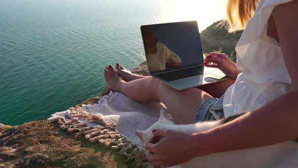 Successful Business Woman in Yellow Hat Working on Laptop By the Sea at Sunset Time