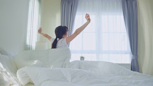 Asian woman wake up from bed and stretching, enjoy early morning after wake up in room at home.