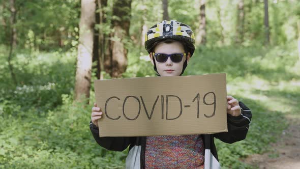 Boy in Sunglasses Helmet Turns Over Cardboard Sign with Monkeypox and Covid19