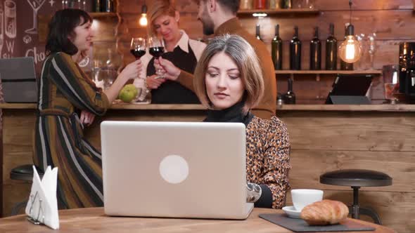 Woman Typing on Her Laptop While People Are Chatting at the Bar