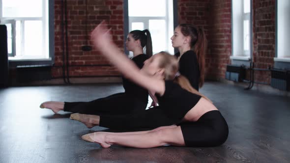 Fitness  Three Young Flexible Women Sitting on the Floor and Stretching for Their Tiptoes One By One