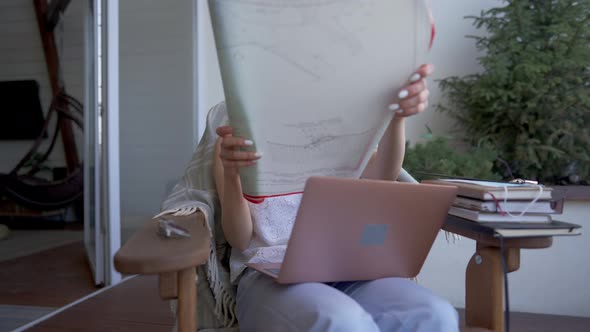 Focused Talented Beautiful Woman Sitting on Armchair with Laptop Receiving Architectural Blueprint