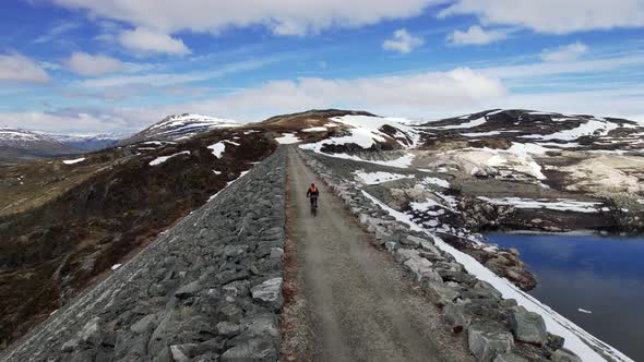 Aerial Follow Shot Behind Male Cycling Across Sysendammen In The Municipality Of Eidfjord in Hordala