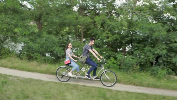 A young couple rides a tandem two-seater bike along the riverbank