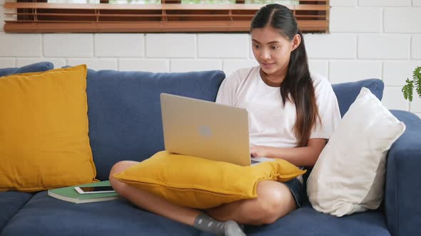 Young Asian happy woman relaxing at home using laptop on a sofa in the living room.