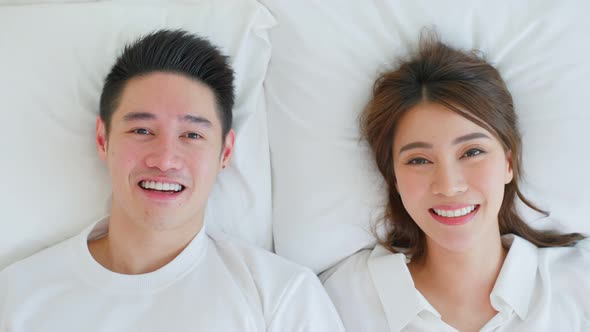 Portrait of Asian new marriage couple lying on bed and look each other.