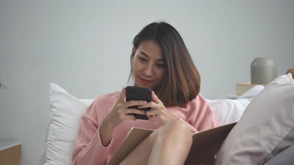 Happy young asian woman studying at home reading an sms or text message on her mobile phone.