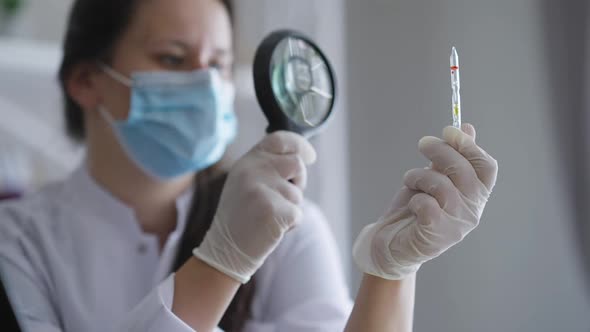 Vax Ampoule and Magnifying Glass in Hands of Blurred Caucasian Young Doctor Examining Medication