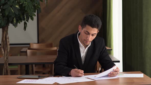 Concentrated Young Arab Businessman Looking Through Marketing Research Report Analyzing Statistical