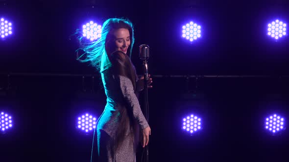 Portrait of a Beautiful Singer with a Vintage Microphone on a Background of Blue Lights. Young Woman