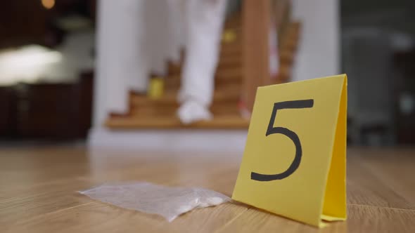 Transparent Package with Pills Lying at Numbered Marker with Blurred Investigator in White Uniform