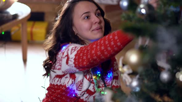 Joyful Young Slim Woman Singing Decorating New Year Tree with Christmas Lights Indoors