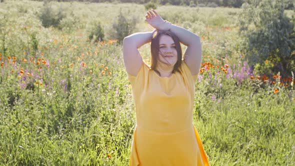 Body Positive Young Fat Beautiful Woman in a Yellow Dress Dances Against the Background of a Field