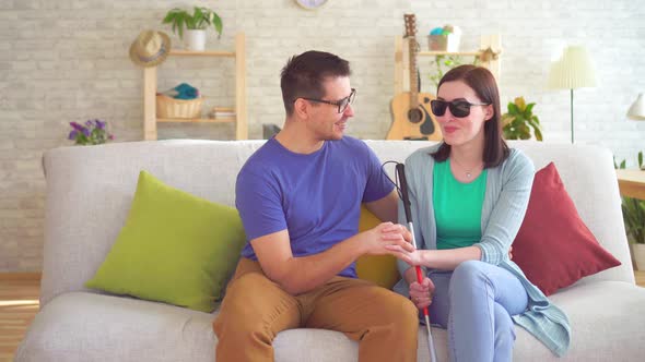 Young Man Flirts with a Blind Disabled Woman Sitting on a Sofa