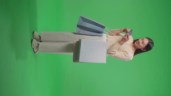 Full View Of Asian Woman With Shopping Bags Enjoy Using Mobile Phone Shopping Online On Green Screen