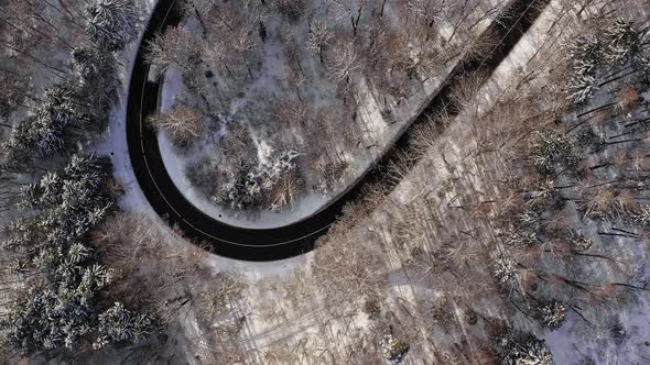 Winter serpentine road - aerial topdown view at a driving car from above on a winding street, look u