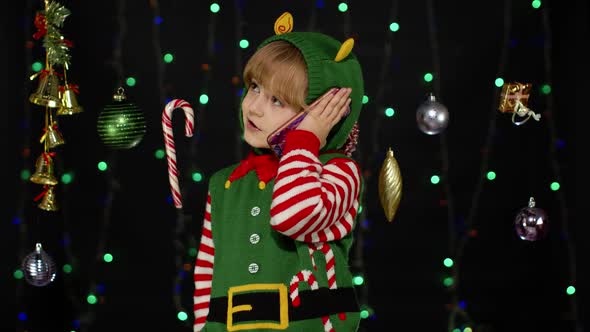 Kid Girl in Christmas Elf Santa Claus Helper Costume Making Congratulations Call on Mobile Phone