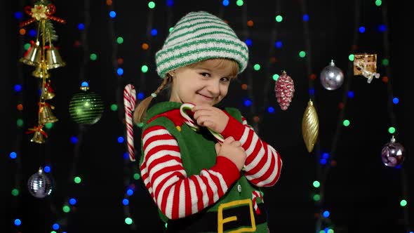 Kid Girl in Christmas Elf Santa Claus Helper Costume Licking Candy Cane Lollipop Caramel Sweets