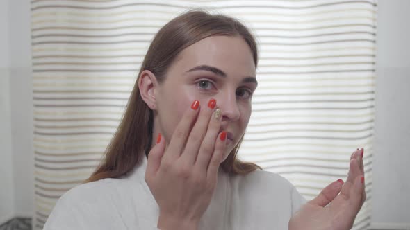 Attractive Young Woman with Heterochromia Looking in the Camera Applying the Daily Cream on Her Face