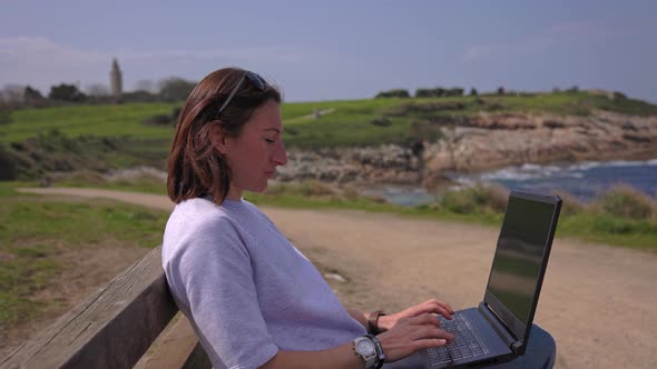 The Girl Works at a Laptop Near the Ocean