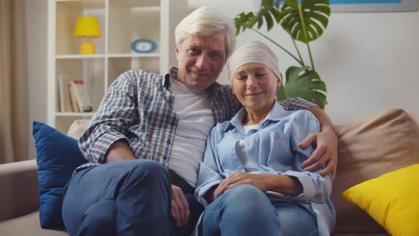 Smiling Woman with Cancer Hugging Husband Sitting on Couch at Home