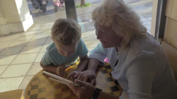 Child and Grandma Using Tablet PC in Cafe