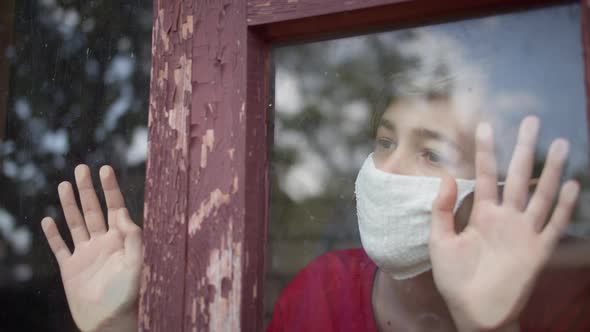 Boy in Mask Sits Inside Looks at the Window and Takes Off the Mask