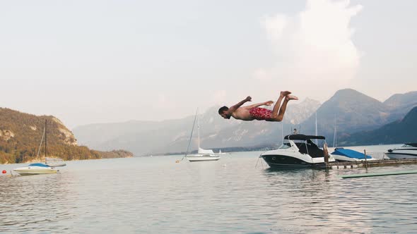 Young Man Jumping Into the Water From Diving Board in Mountain Lake Slow Motion