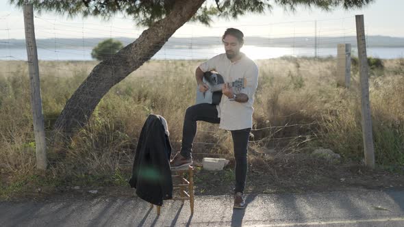 Spanish Macho Man Strumming on Acoustic Guitar Standing Roadside and Sing Song Looking at Camera at