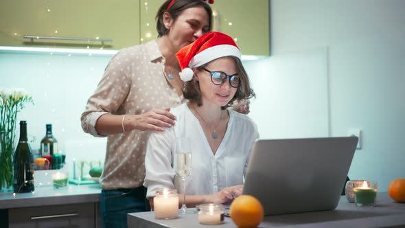 Two Young Women Drinking Champagne While Talking with Friends Via a Video Call