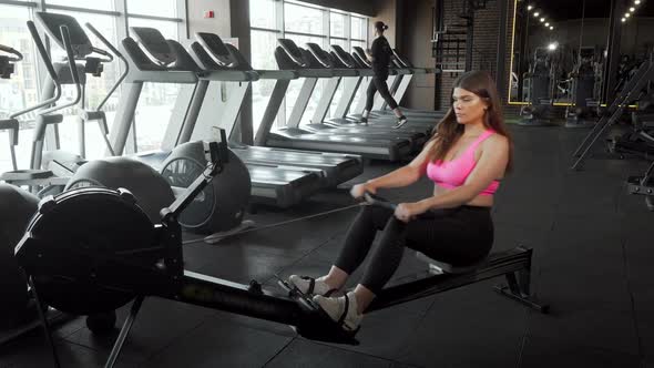 Beautiful Curvy Sportswoman Working Out on Rowing Machine at the Gym