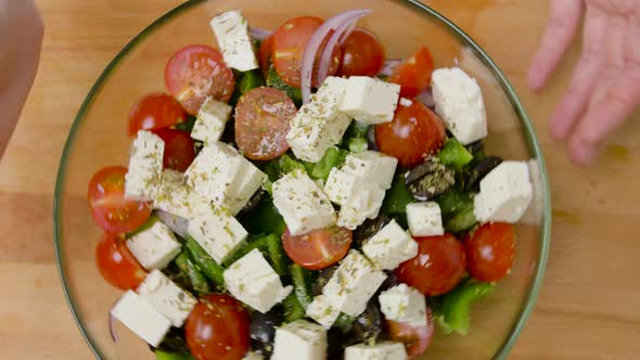 Hands Turning Bowl of Vegetable Salad with Feta