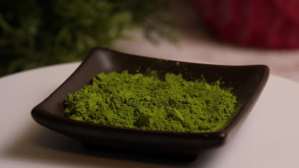 Green matcha tea powder in a dish rotating on a white plate