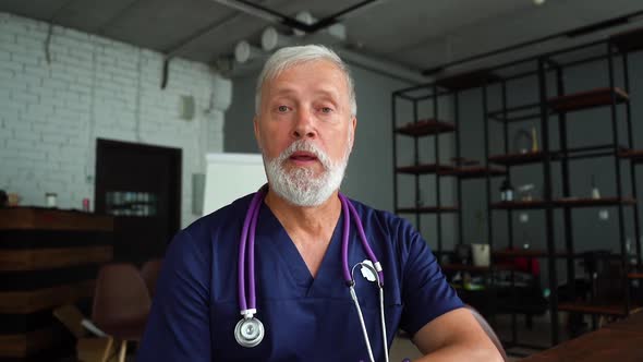 Senior Gray-haired Mature Male Doctor Consulting of Patient Via Internet Looking at Webcam.