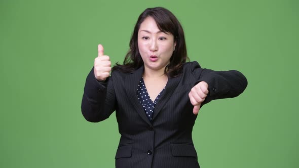 Mature Confused Asian Businesswoman Giving Thumbs Up and Thumbs Down