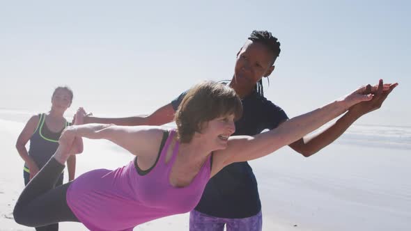 African American yoga teacher woman helping woman on the beach and blue sky background