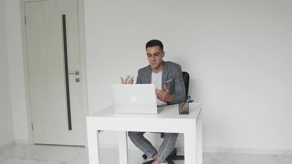 Male Student in a Suit Chatting Online on a Laptop at Table Remotely Indoors