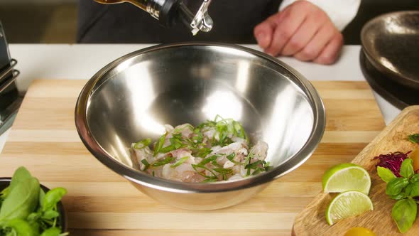 Professional Chef Adding Oil to Raw White Fish Fillet in Metal Bowl on Cutting Board Closeup