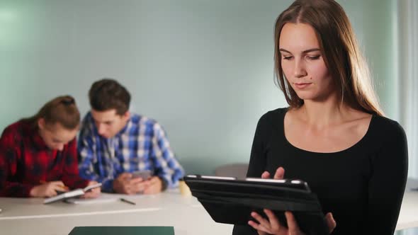 An Attractive Young Woman Standing in the Office and Using Her Tablet While Her Colleagues are
