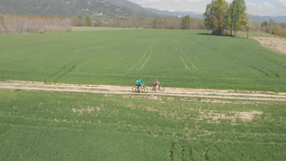 Couple having fun by riding mountain bike on dirt road in sunny day, scenic landscape of snowcapped